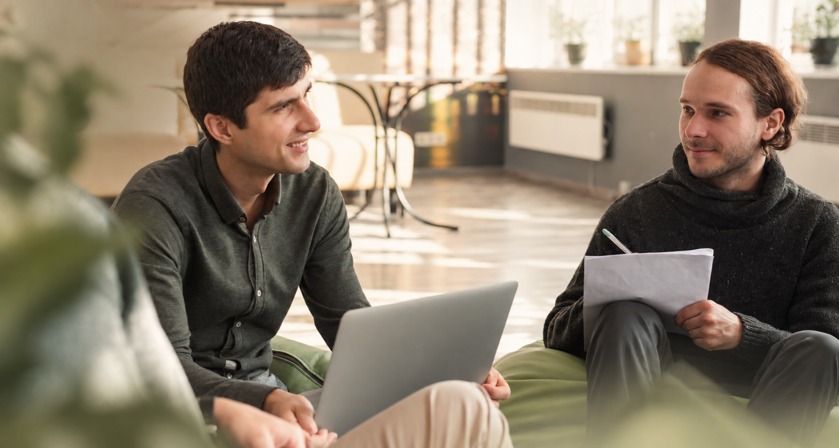 Zwei Menschen sprechen in einer Arbeitslounge bei einem Laptop über ein Projekt